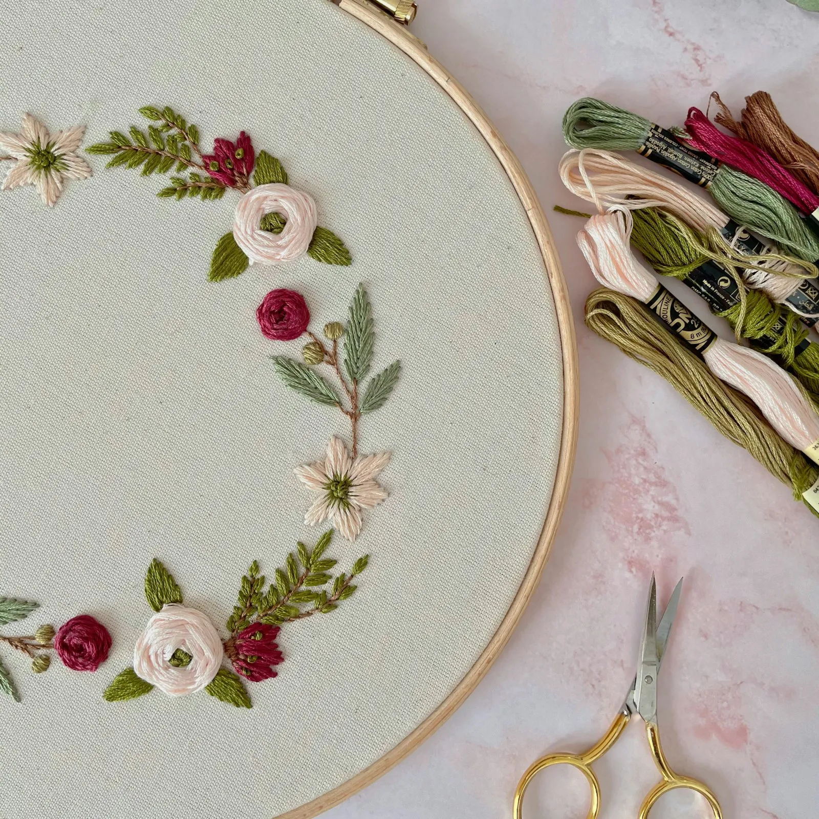 Broderiramme med en krans av roser og blader, og broderigarn ved siden av